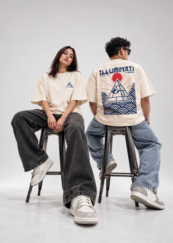 Two models sitting on stools in a studio setting, wearing cream-colored t-shirts. The model on the left shows the front of the shirt with a small blue triangle logo, while the model on the right shows the back of the shirt with a large blue pyramid graphic and red sun design.