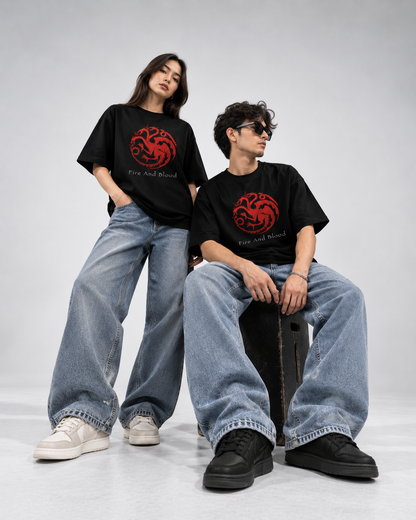 A man and a woman modeling matching black graphic t-shirts with a red dragon emblem and the words 'Fire and Blood' printed on the front, paired with wide-leg light blue jeans.