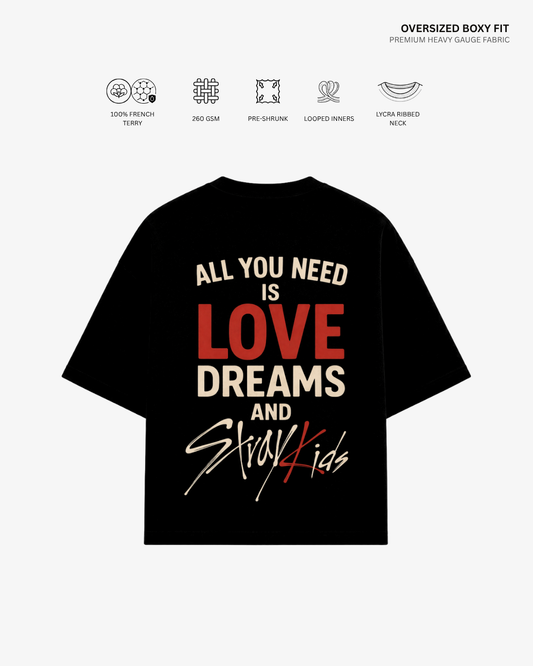 A black oversized boxy-fit t-shirt with a graphic print on the back, featuring the text 'ALL YOU NEED IS LOVE DREAMS AND Stray Kids' in cream and red. The image includes feature icons and text at the top describing the fabric and fit details.