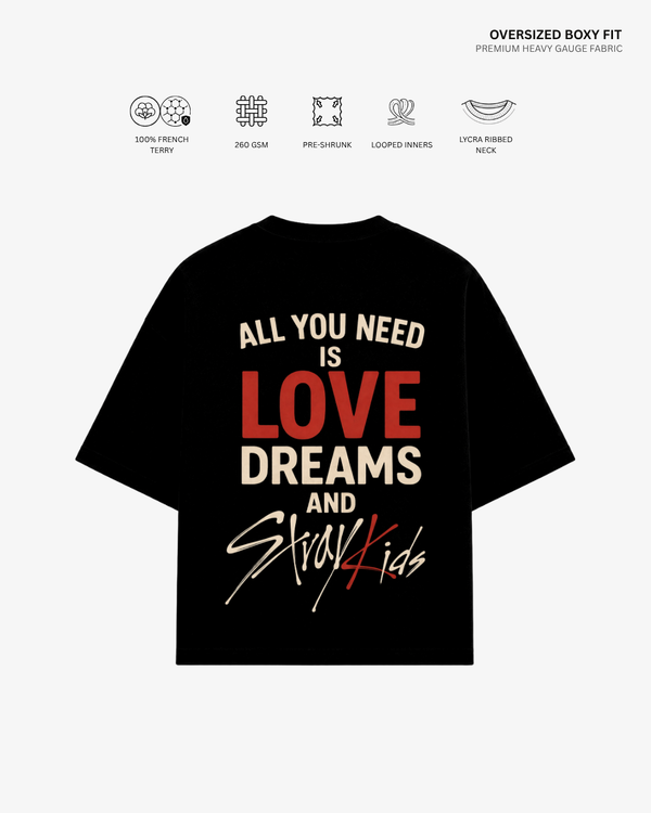 A black oversized boxy-fit t-shirt with a graphic print on the back, featuring the text 'ALL YOU NEED IS LOVE DREAMS AND Stray Kids' in cream and red. The image includes feature icons and text at the top describing the fabric and fit details.
