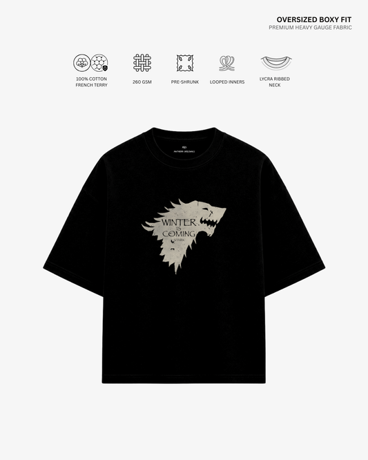 A black oversized short-sleeve T-shirt with a large light beige 'Winter is Coming' direwolf graphic on the front, shown on a light gray background with feature icons and text above.